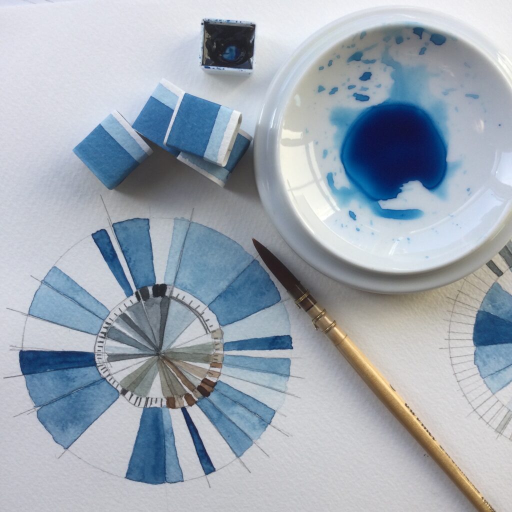 Prussian Blue watercolour painting with Art Scribe. Image shows a mixing palette with blue watercolour paint, a paint brush, cubes of handmade watercolour paint and a colour mixing chart with Prussian Blue mixed with black and burnt umbre.