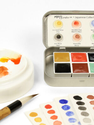 Open tin of Japanese Handmade Watercolour Collection by Art Scribe sits on the table with a paintbrush, paint palette and gradients of the six colours.
