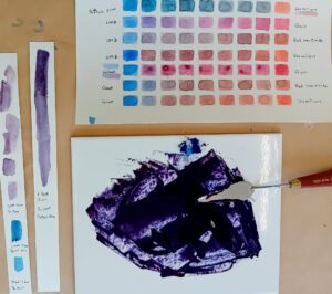 Image shows a watercolour mixing chart and test stripes with notations. On a white tile is a palette knife with a purple coloured paint being made.
