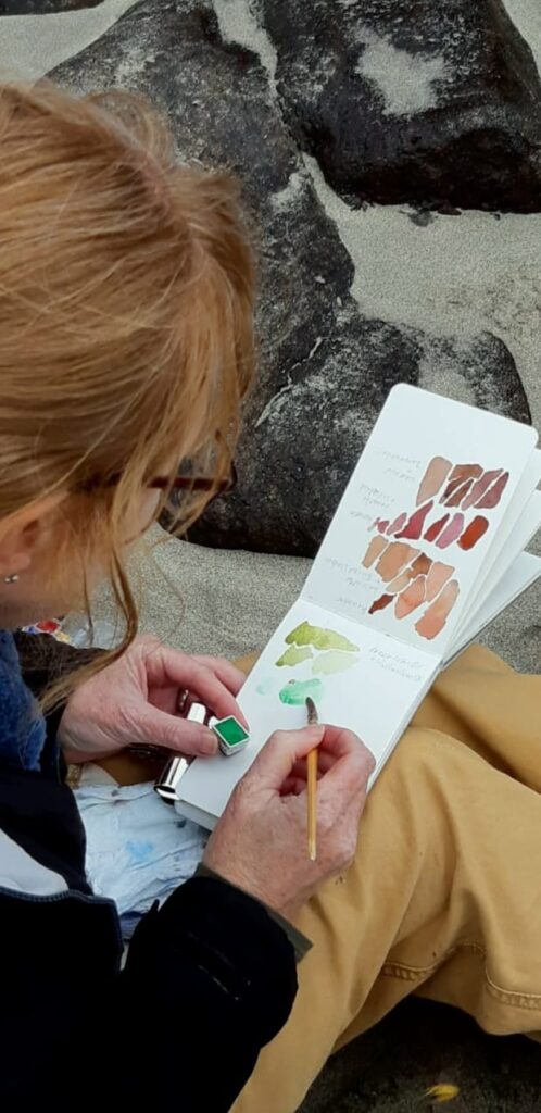 seated figure paints the colours in their sketchbook.